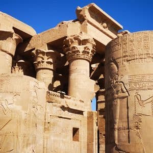 Alte Sandsteintempelruinen mit Säulen und hieroglyphischen Schnitzereien unter einem leuchtend blauen Himmel.