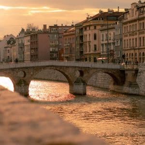 Un ponte ad arco in pietra attraversa un fiume in una città, con l'acqua che riflette la luce dorata del tramonto.