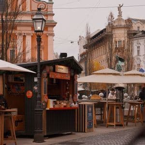 An outdoor market stall and seating area on a cobblestone street in a historic city square under an overcast sky.