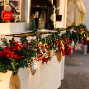 A close-up of a Christmas garland with small ornaments hanging from the front of a white wooden counter at an outdoor stall.