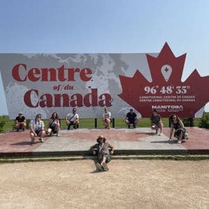 Un viaggio di gruppo WeRoad in posa per una foto davanti al grande cartello 'Centre of Canada' in Manitoba.