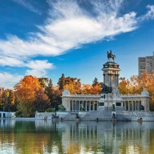 Un monumento in pietra con colonnato e statua equestre sorge accanto a un laghetto circondato da alberi autunnali