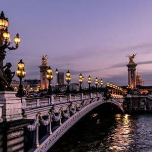 Un ponte di pietra decorato con lampioni d'epoca luminosi e sculture dorate che attraversa un fiume al crepuscolo