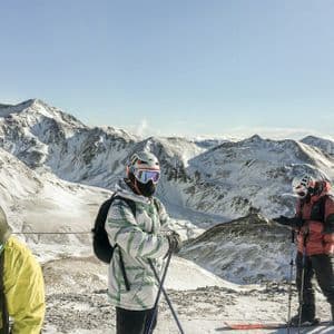 Un viaje en grupo de WeRoad de esquiadores con casco y gafas en la cima de una montaña nevada en un día despejado.