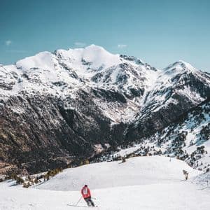 Un esquiador con chaqueta roja se desliza por una pendiente nevada con un fondo de montañas agrestes y cubiertas de nieve.