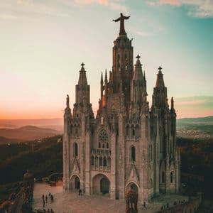 Una catedral de piedra con altas agujas y una estatua en la cima se alza sobre una colina contra un cielo al atardecer.