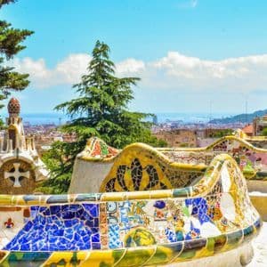 Bancos curvos de mosaico colorido dominan el extenso horizonte de la ciudad y el mar lejano bajo un cielo azul.