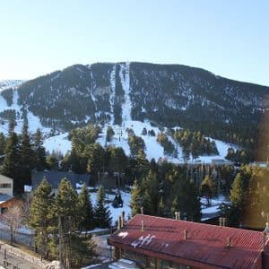 Las pistas de esquí cubiertas de nieve y los telesillas cruzan una montaña boscosa que se eleva sobre un pueblo con tejados de chalets.