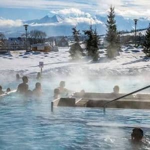 A WeRoad group trip of people soaking in a steaming outdoor thermal pool surrounded by snow and mountains.