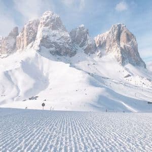 Neve battuta su una pista da sci che conduce verso imponenti cime montuose rocciose innevate sotto un cielo limpido.