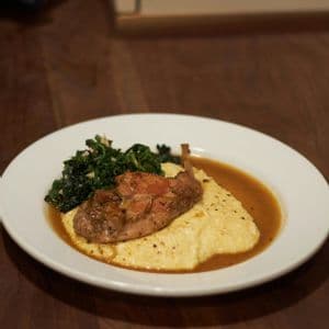 Un piatto di carne arrostita servita su polenta cremosa con verdure saltate e sugo su un tavolo di legno