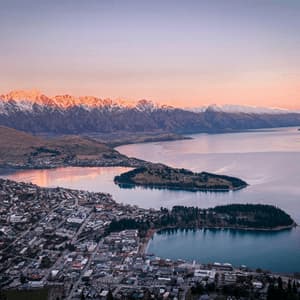 Vista aerea di una cittadina lacustre che confina con l'acqua e penisole boscose con montagne innevate che risplendono all'alba