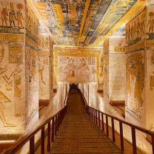 Una rampa di legno scende attraverso un'antica tomba fiancheggiata da colonne dipinte, geroglifici e colorati murales sul soffitto.