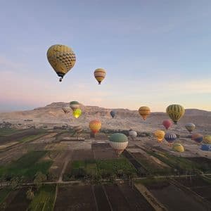 Colorate mongolfiere fluttuano su campi coltivati e colline aride sotto un dolce cielo mattutino