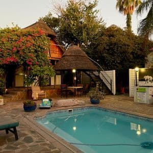 Una piscina in un cortile in pietra circondata da lussureggiante vegetazione, padiglioni con tetti di paglia e posti a sedere all'aperto.