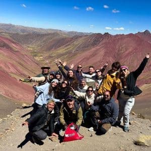 Un viaggio di gruppo WeRoad in posa allegra su una cima di montagna con valli rossastre sullo sfondo