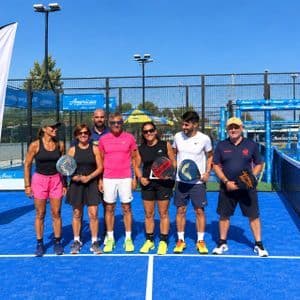 Un gruppo di giocatori di padel in posa con le racchette su un campo all'aperto blu brillante sotto un cielo sereno