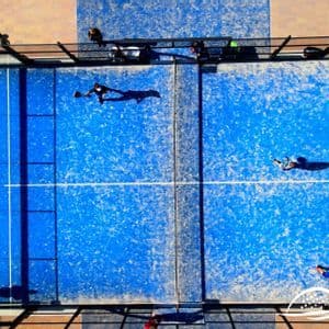 Vista aerea dall'alto di persone che giocano una partita su un campo da padel all'aperto blu vibrante.