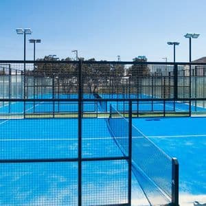 Campi da padel blu esterni vuoti recintati da reti in metallo nero sotto un cielo limpido e soleggiato