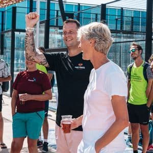A WeRoad group trip smiling and celebrating together outdoors by a padel court on a sunny day.