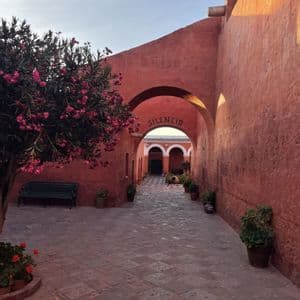 Cortile rosso terracotta con pavimentazione in pietra, albero in fiore rosa e un arco contrassegnato dalla parola SILENCIO.