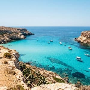 Un viaggio di gruppo WeRoad cammina lungo un sentiero costiero roccioso che domina una caletta dal mare turchese con barche ancorate.