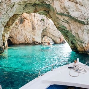 Una barca naviga attraverso acqua turchese sotto archi marini di pietra naturale e formazioni rocciose.