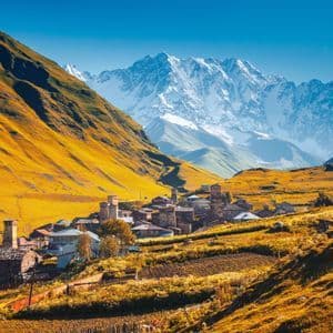 Pueblo de piedra con torres medievales enclavado en un valle bajo picos de montañas nevados bajo un cielo azul despejado