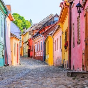 Une étroite rue pavée serpente entre des bâtiments historiques aux couleurs vives sous un ciel clair.