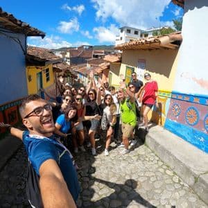Eine WeRoad Gruppenreise macht ein lächelndes Selfie auf einer engen Kopfsteinpflastergasse zwischen farbenfrohen Gebäuden.