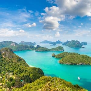 Vista aérea de un archipiélago con exuberantes islas verdes en aguas turquesas bajo un cielo azul con nubes.