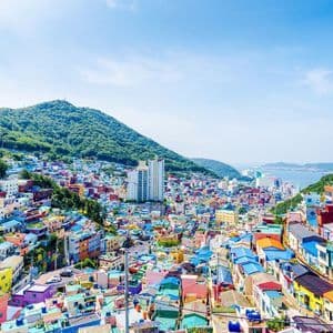 Una vista panoramica di un villaggio con edifici dai colori vivaci che scendono a cascata lungo un rigoglioso versante verde verso il mare.