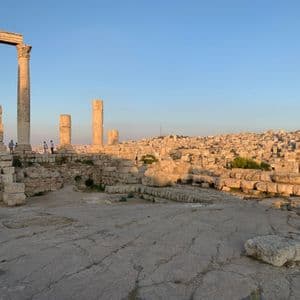 Un groupe WeRoad se tient parmi d'anciennes ruines de pierre aux hautes colonnes, surplombant une ville étendue sur une colline au coucher du soleil.