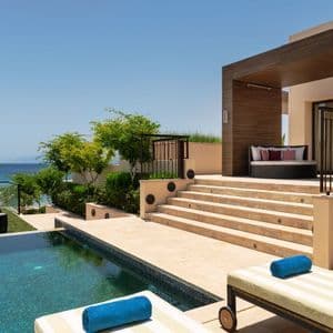 Un patio de hotel moderno con piscina y tumbonas tiene vistas al mar azul tranquilo bajo un cielo despejado.