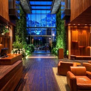 Le hall d'un hôtel moderne avec boiseries, jardins verticaux illuminés et un coin salon avec fauteuils en cuir.