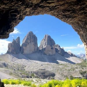 Jagged mountain peaks viewed from inside a rock cave, framed by its arch against a blue sky.