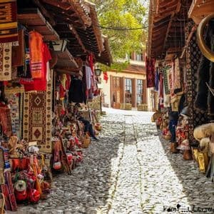 Una stretta strada acciottolata fiancheggiata da bancarelle all'aperto che vendono tappeti colorati e artigianato locale.