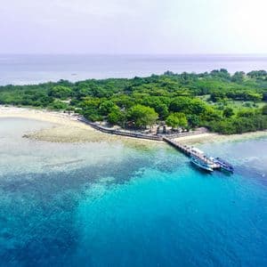 Vue aérienne d'une petite île tropicale avec une jetée en bois où deux bateaux sont amarrés dans une eau turquoise.