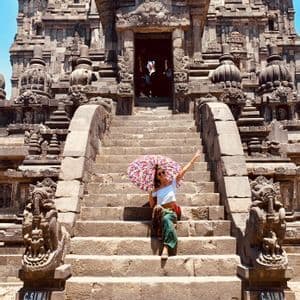 Una mujer con un paraguas colorido y estampado se sienta en los anchos escalones de piedra de un antiguo templo ornamentado.
