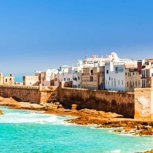 Una ciudad fortificada con edificios encalados en una costa rocosa con agua turquesa bajo un cielo despejado.