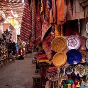 Une ruelle pavée étroite dans un marché couvert, avec des étals exposant des céramiques colorées, des tapis à motifs et d'autres articles.