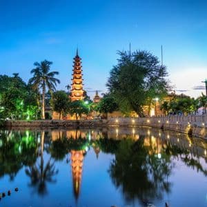 Une tour de pagode illuminée et les arbres environnants se reflétant dans l'eau calme au crépuscule.