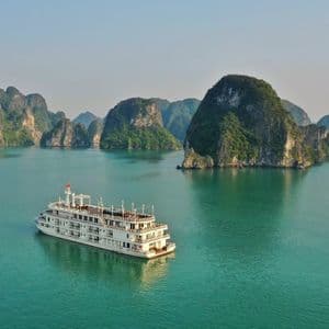 Un grand navire de croisière blanc navigue sur une eau turquoise calme parmi d'imposants karsts calcaires couverts de verdure.