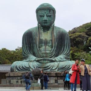 Una gigantesca estatua de bronce de Buda, sentado, se erige sobre turistas que toman fotos en un patio al aire libre.