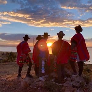 Un viaje en grupo de WeRoad, vestidos con ponchos y sombreros rojos, observa el atardecer desde una colina con vistas a un gran lago.