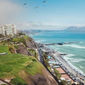 Una vista aérea de una ciudad costera en acantilados, con varios parapentistas volando sobre el océano y un muelle.