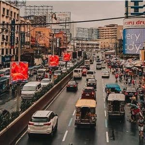 Vogelperspektive auf eine verstopfte Stadtstraße mit Autos, Jeepneys und Bussen auf nasser Fahrbahn und Fußgängern auf den Gehwegen.