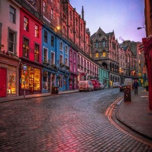 Une rue pavée sinueuse bordée de bâtiments historiques colorés aux fenêtres lumineuses sous un ciel crépusculaire.