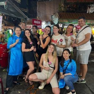 Un gruppo WeRoad in viaggio posa per una foto in un mercato notturno, con molti membri che tengono in mano fiori di loto rosa.