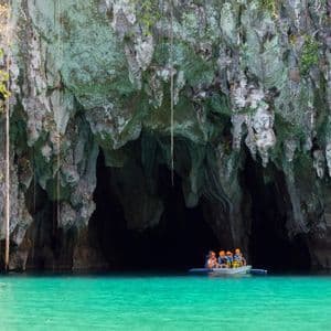 Eine WeRoad Gruppenreise in einem kleinen Boot am Eingang einer großen Meereshöhle mit türkisfarbenem Wasser.